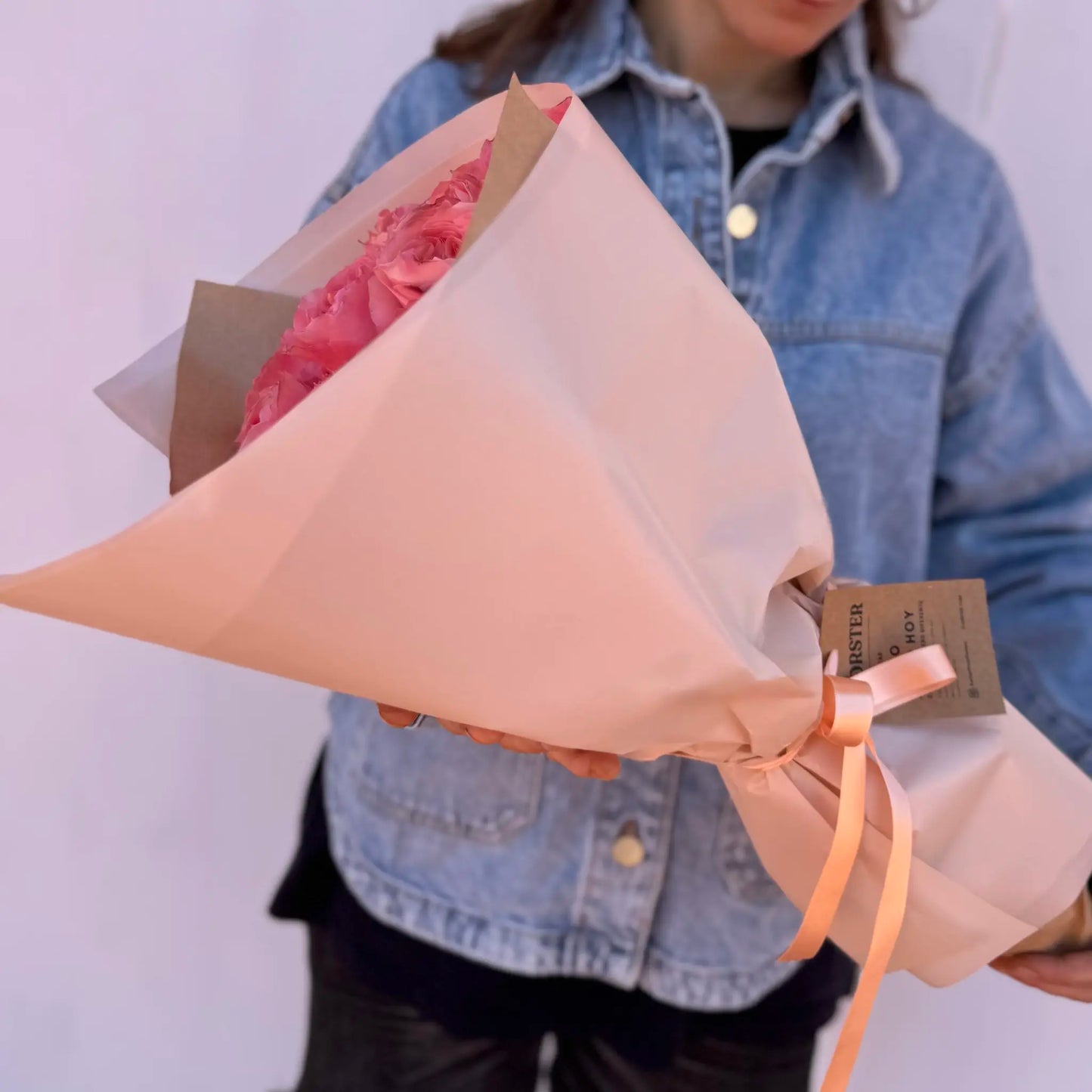 Person holding a bouquet of pink garden roses flowers wrapped in brown paper with a visible brand tag Florster Barcelona.