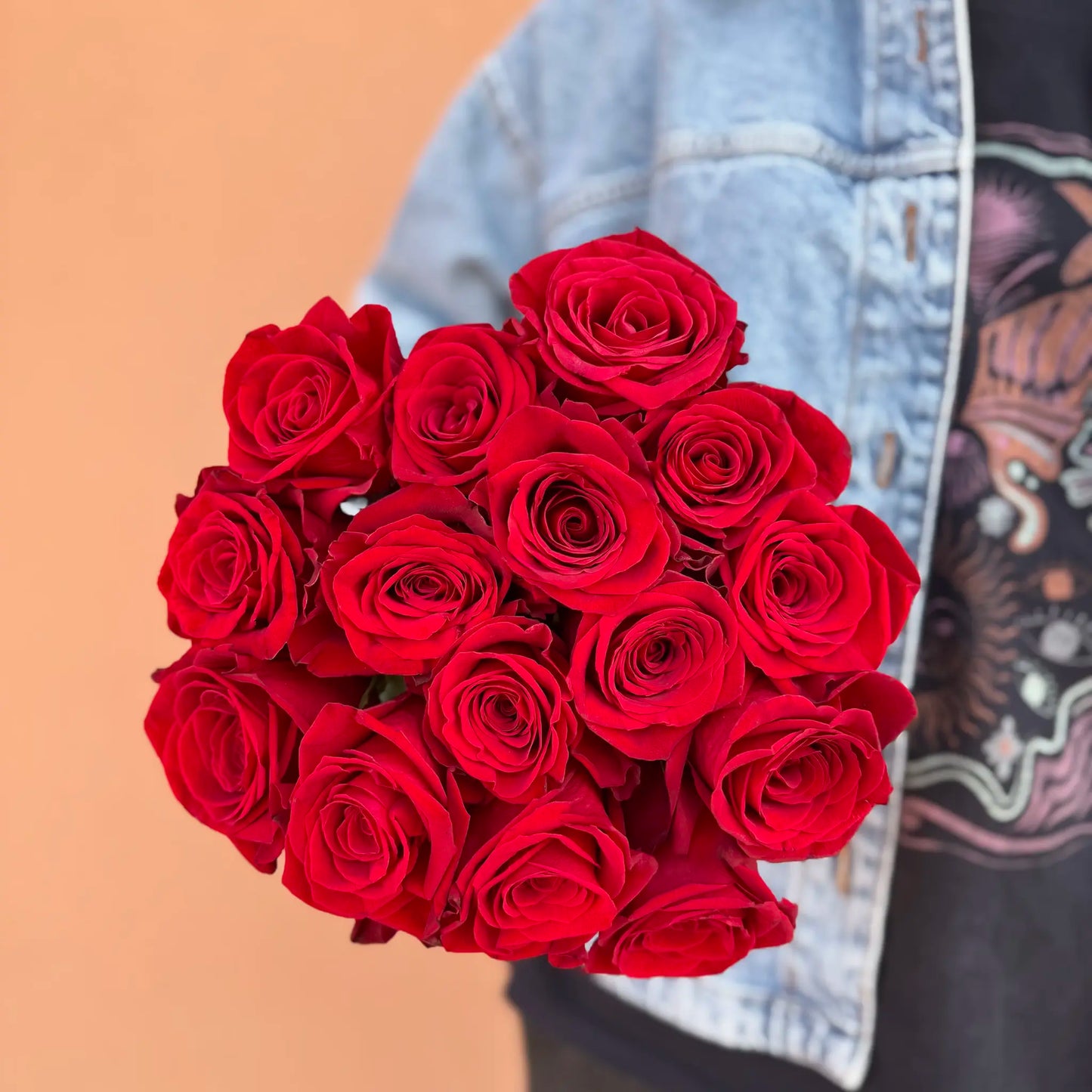 Bouquet of red roses held by a person wearing a denim jacket.
