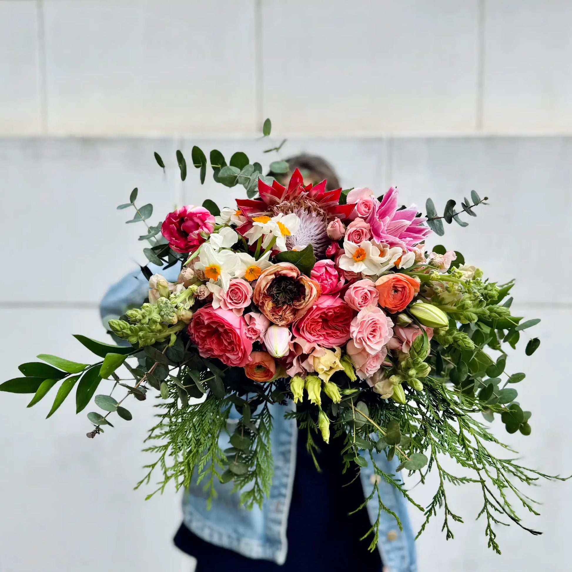Person holding a vibrant bouquet of flowers against a light background