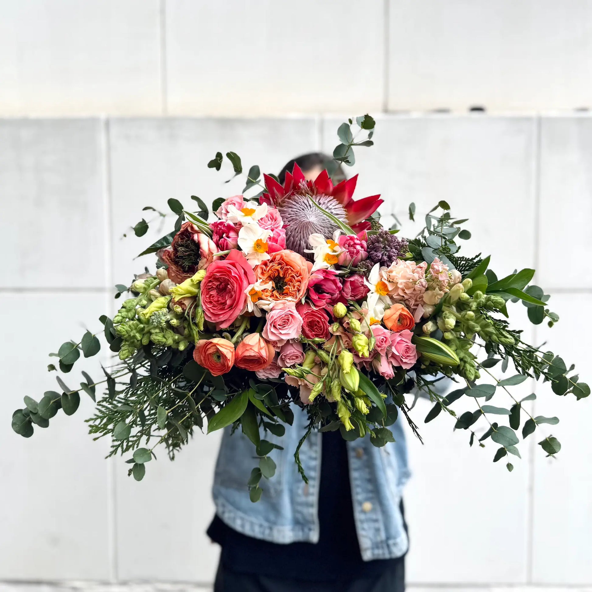 Person holding a vibrant big bouquet of flowers against a white tiled wall