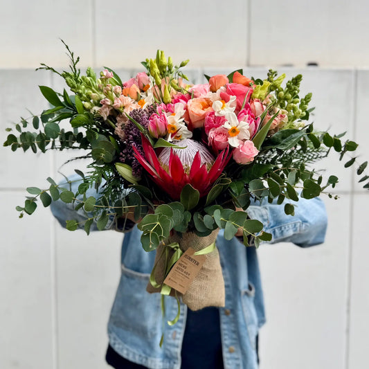Big Bouquet of flowers held by a person wearing a denim jacket against a white tiled wall.