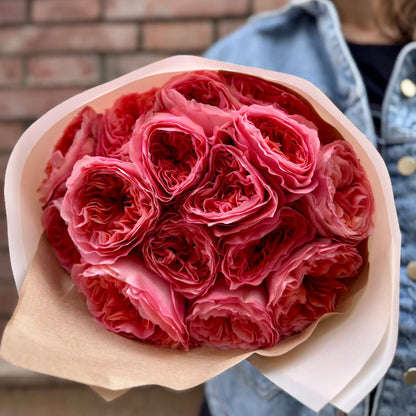 Bouquet of pink roses wrapped in brown paper held by a person wearing a denim jacket.