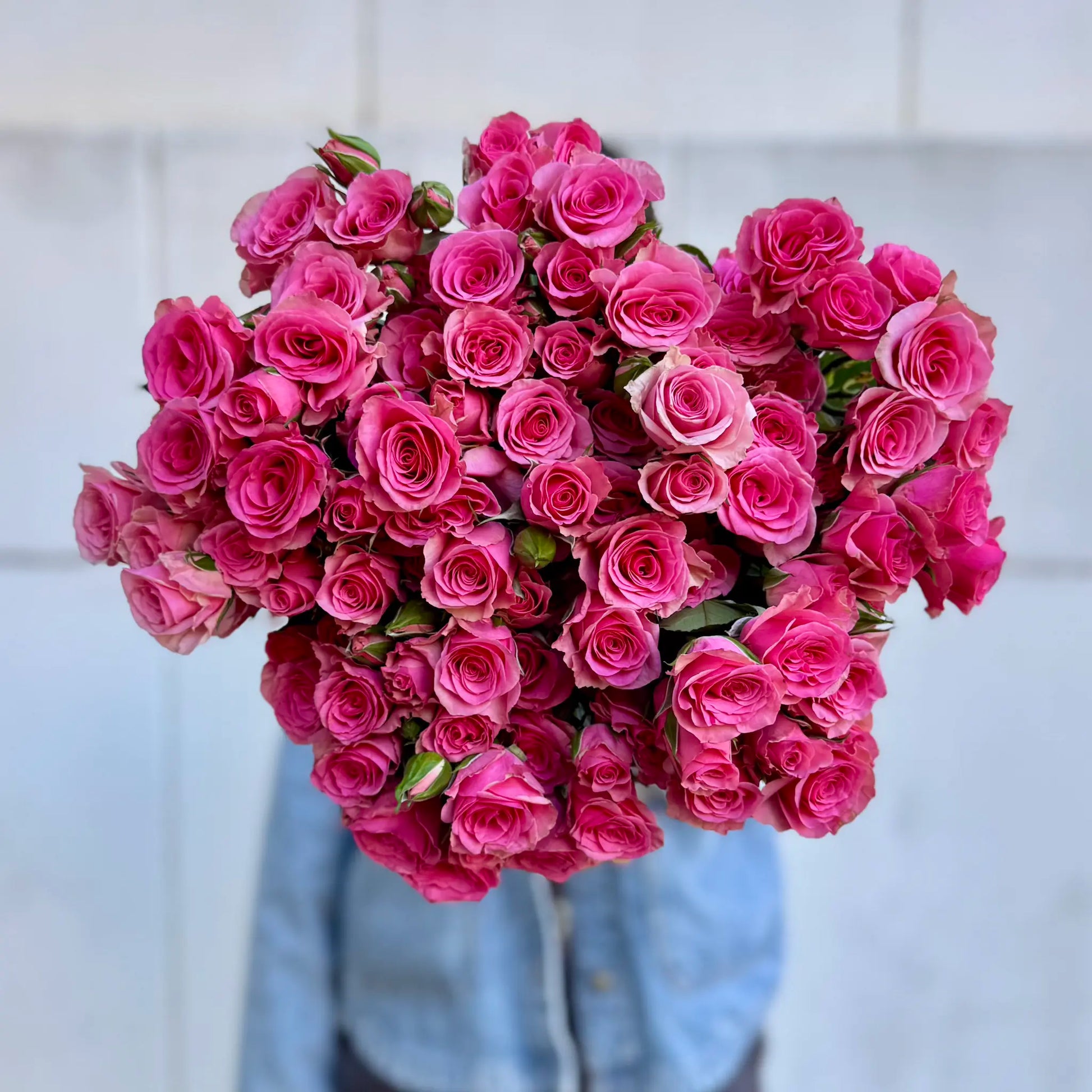 Bouquet of pink spray roses held by a person wearing a denim jacket.