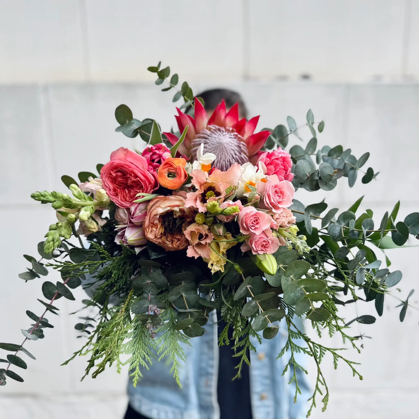 Bouquet of flowers with greenery held by a person against a light background