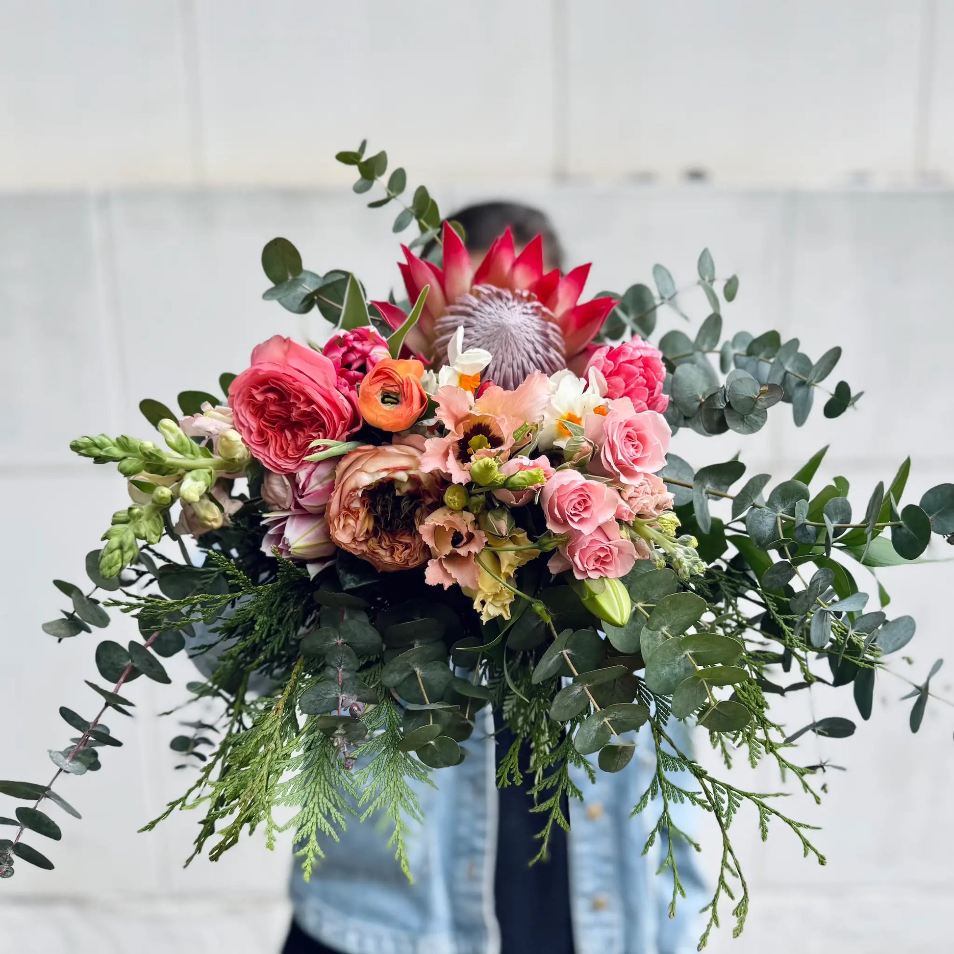 Bouquet of flowers with greenery held by a person against a light background