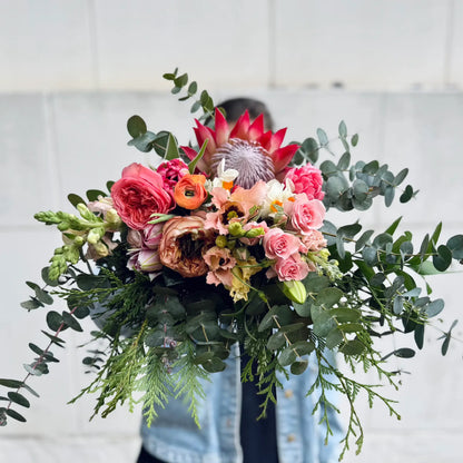 Bouquet of flowers with greenery held by a person against a light background