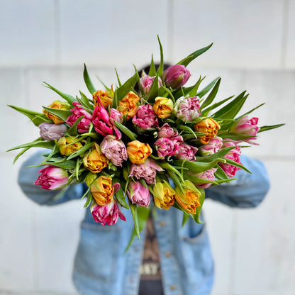 Bouquet of colorful tulips held by a person wearing a blue jacket against a light background