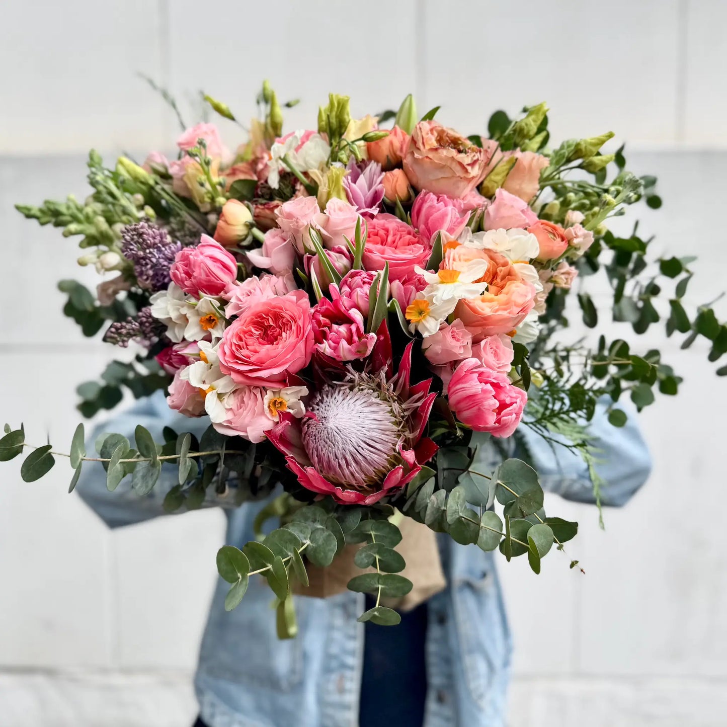 Bouquet of pink and green flowers held by a person wearing a denim jacket.