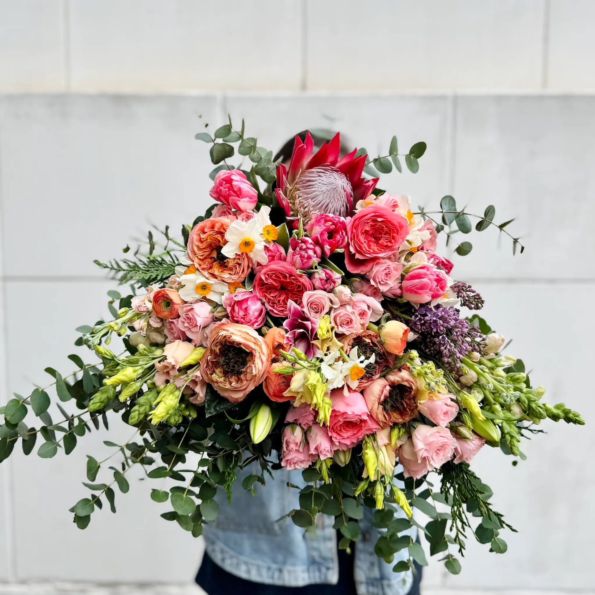 Bouquet of colorful flowers held by a person against a light gray tiled wall.