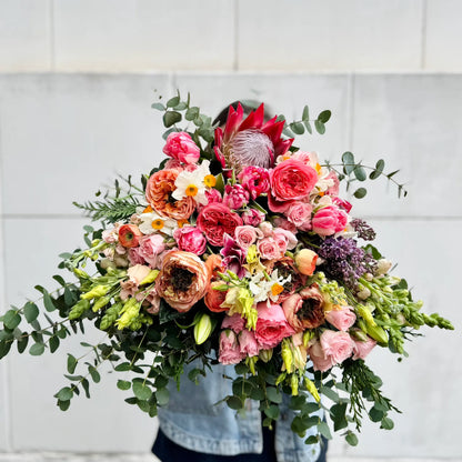 Bouquet of colorful flowers held by a person against a light gray tiled wall.